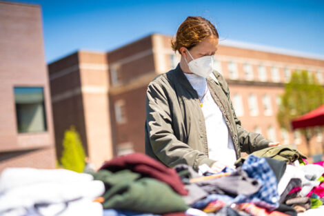 student in mask looks at clothing available at Pop-Up Thrift Shop