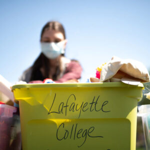 green bin with Lafayette College on it holds donated clothing, student wears mask in background