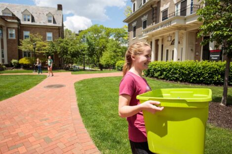 student smiles while carrying green bin outside near residence halls