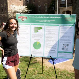 Two students smile at the camera in front of a poster titled "Evaluating Sustainable Efforts in Lafayette Athletics"