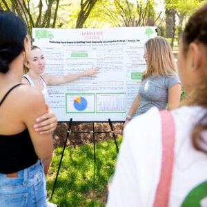 Two students facing away from the camera look at two students in front of a poster board titled "Reducing Food Waste and Battling Food Insecurity at Lafayette College"