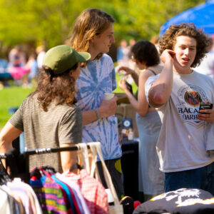 Three students in t-shirts face each other to talk behind a rack of clothing on hangers