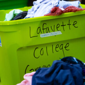 A green plastic bin full of clothes with "Lafayette College" visible on the side in black marker