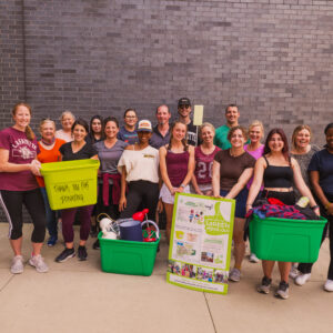 A group of students and staff members smile at the camera while holding green bins and Green Move Out signage