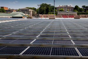 Rows of solar panels extend away from the camera with Oeschle Hall, Markle Hall, and the stands of Fisher Stadium in the background