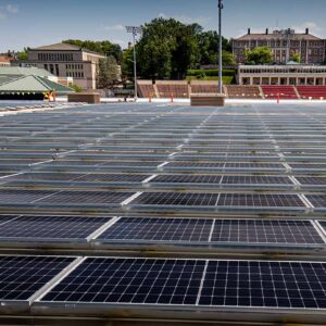 Rows of solar panels extend away from the camera with Oeschle Hall, Markle Hall, and the stands of Fisher Stadium in the background