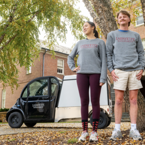 Two students in gray Lafayette Sustainability sweatshirts stand in front of an electric vehicle